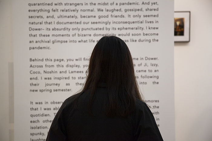 a person with long dark hair standing in front of a very large hanging printout of black text on white paper