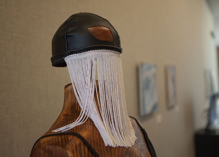 close-up on a black half-face mask on a wooden dress form, with long white fringe