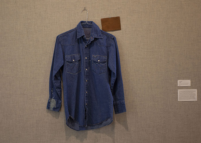 a denim shirt and a leather postcard hung on a grayish fabric wall