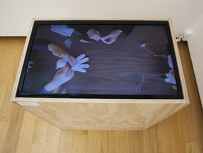 a video of people's hands unravelling gloves, shot top-down, displayed table-top style in a wooden cabinet