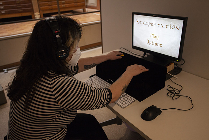 a person in a striped shirt wearing headphones and a mask, playing a computer-based game in front of a monitor