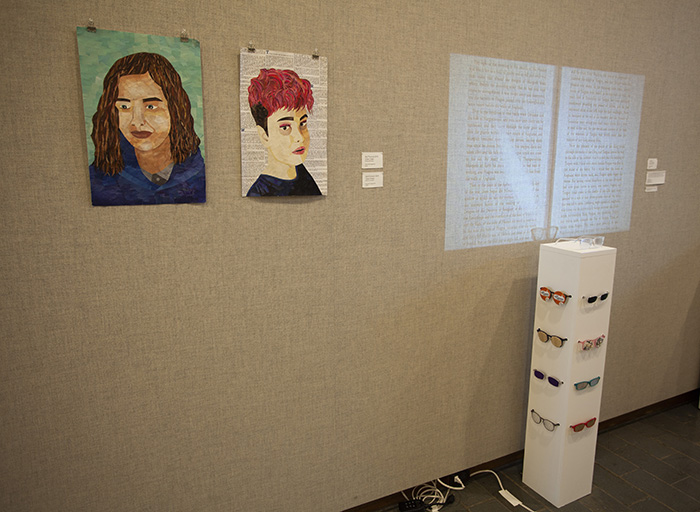 two portrait collages on a grayish fabric wall at left, a pedestal-based sculpture with video projection at right