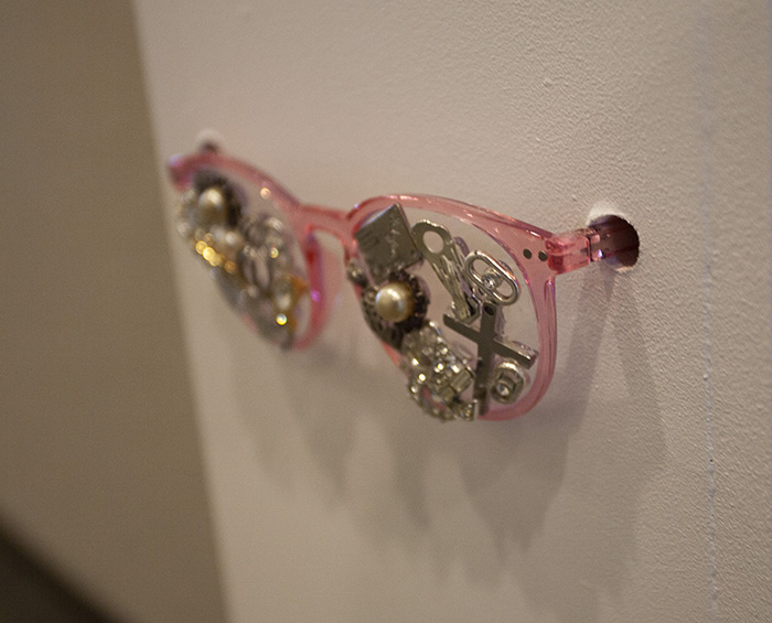 pink-framed glassed installed in the side of a white pedestal, with lenses covered in costume jewelry and metal findings