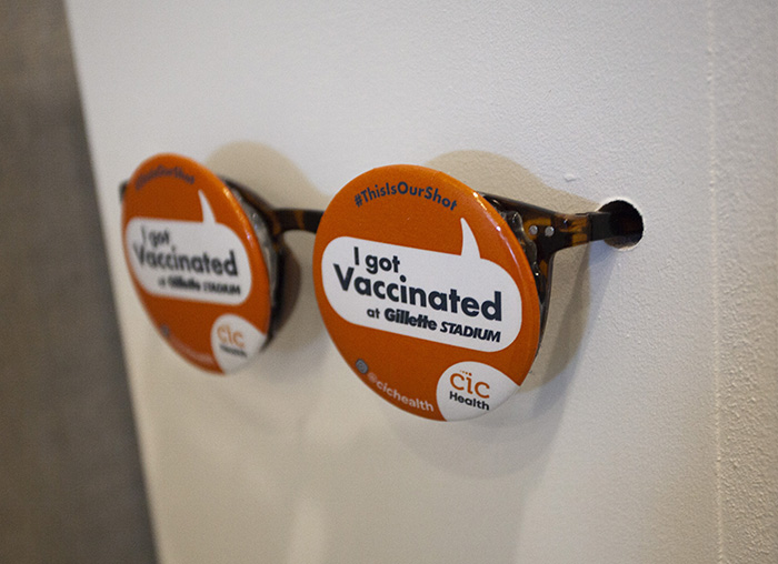 glasses installed in the side of a pedestal, with the lenses replaced by orange 'I got vaccinated at Gillette Stadium' pins