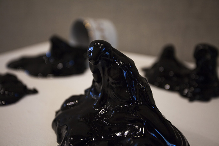 close-up on a sculpture of shiny black good with a blog stretched upwards. Out of focus behind it, more blobs are visible