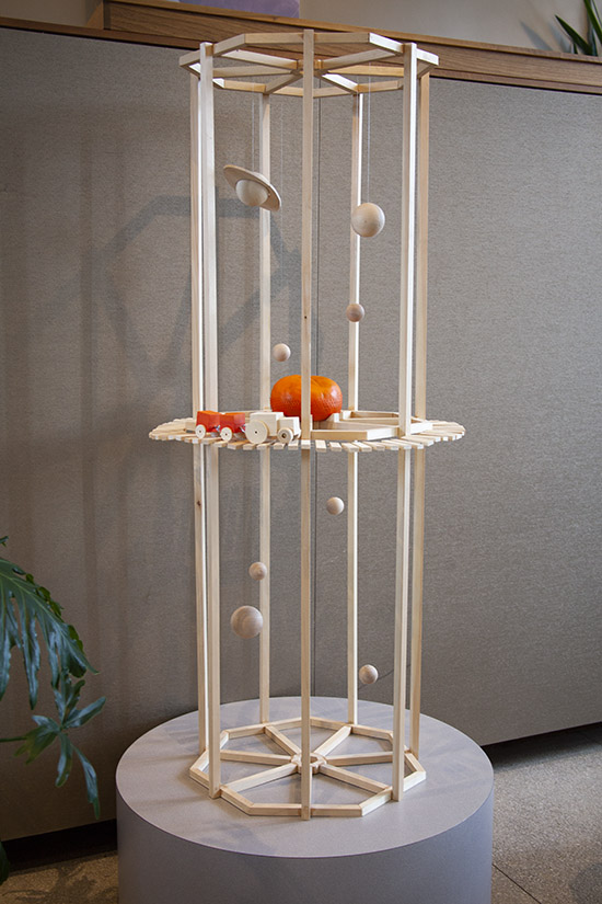 wood sculpture with hanging planets, a train, and a plaster clementine