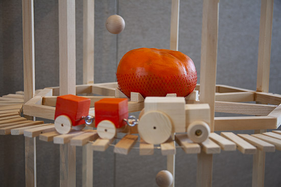 close up on part of a wood sculpture with wood train and orange plaster clementine sculpture