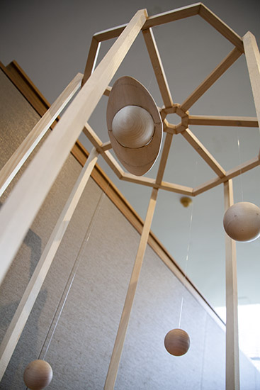 a shot looking up from below at a wooden sculpture with hanging wooden planets