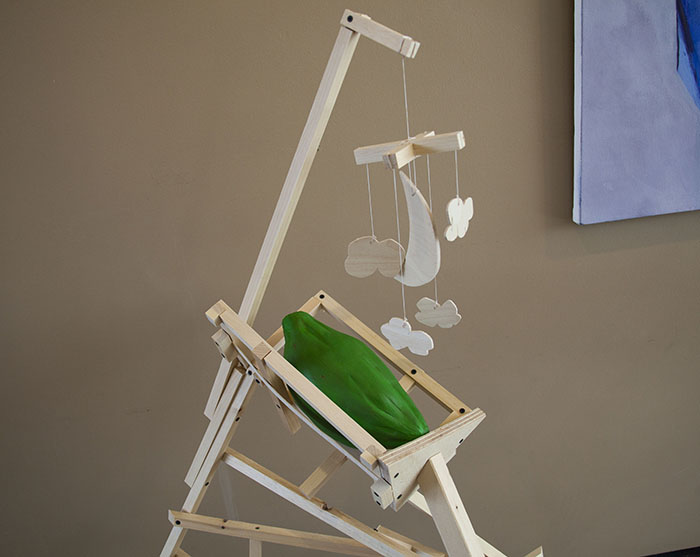 an oversized green plaster payapa in a wooden cradle with a wooden mobile with moon and clouds hanging above it