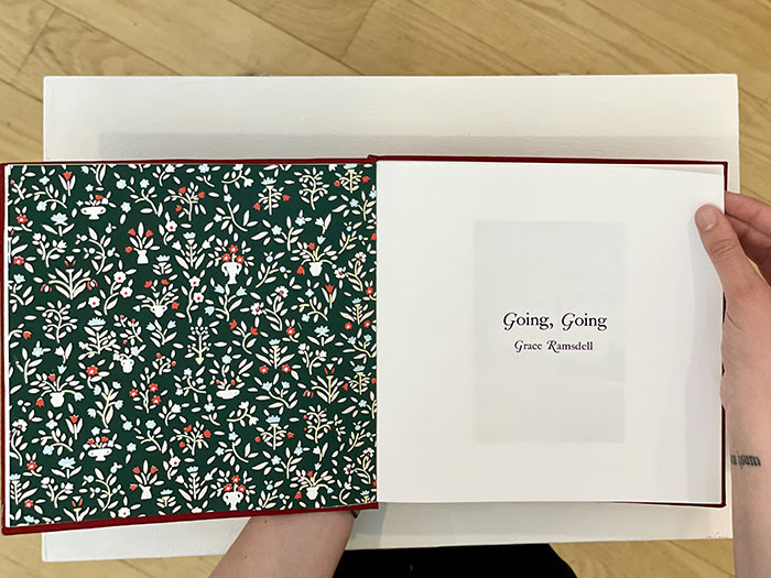 open book; the left page is a green, red, and white floral wallpaper; the right page has the words 'Going, Going' and 'Grace Ramsdell' on it