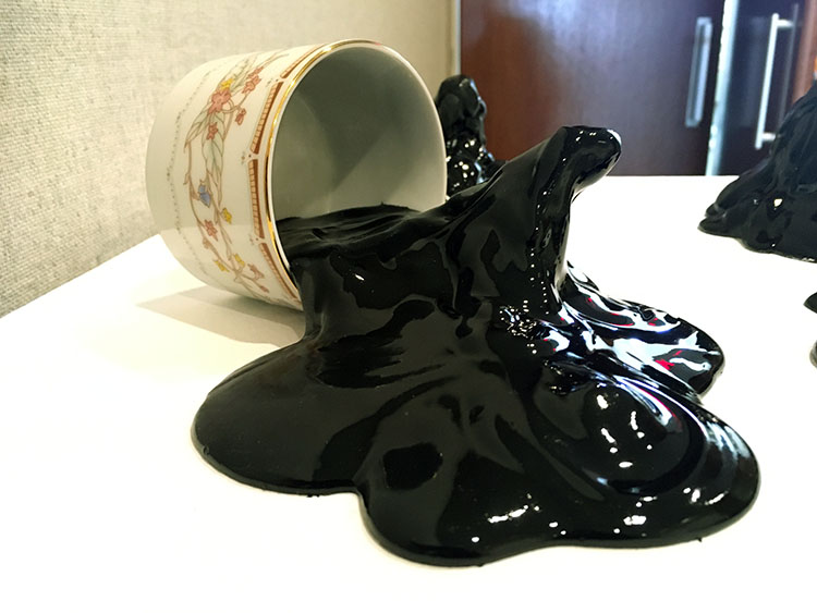 a floral tea cup on its side, with solidified shiny black goo spilling out