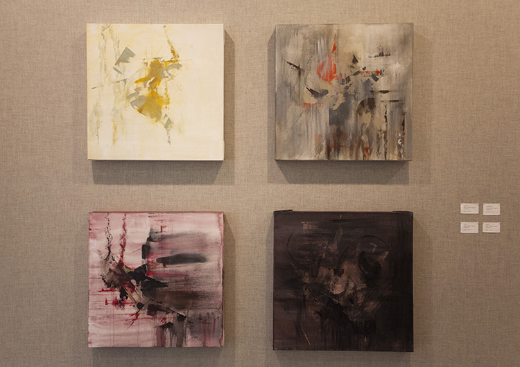 grid of 4 abstract paintings on a gray fabric wall