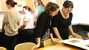 a pair of students studies a print, while three in the background discuss another piece