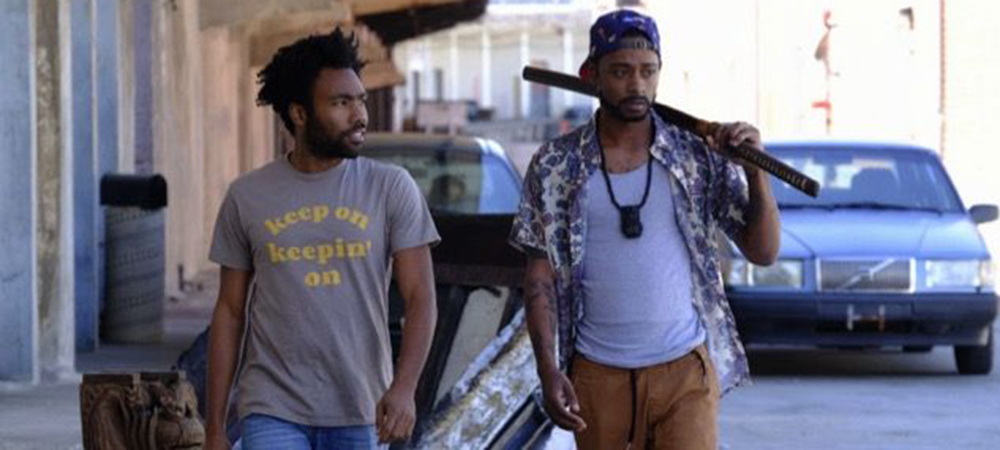 A still from the TV series Atlanta, two men are walking down the street, one of them is holding a bat