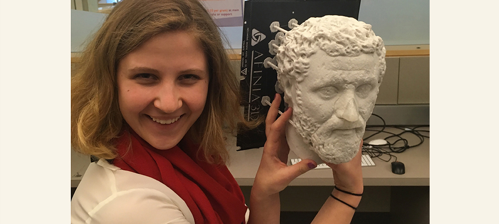 Student holding a Greek statue head replica next to her head and smiling