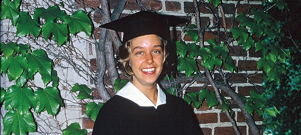 Young Betsy wearing a cap and gown in front of an ivy-covered wall