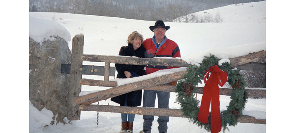 Betsy and Bud in front of a snowy landscape and behind a gate with a Christmas wreath