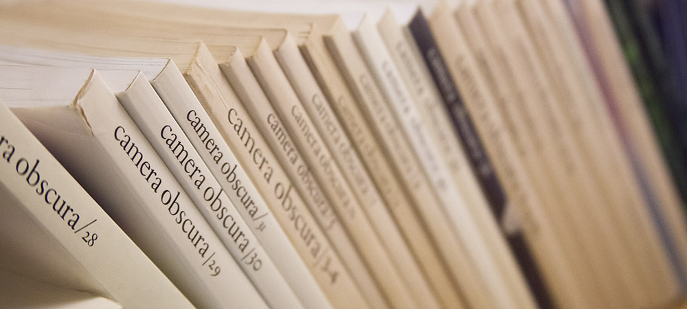 close-up photo of many small publications upright on a shelf with 'camera obscura' down their spines