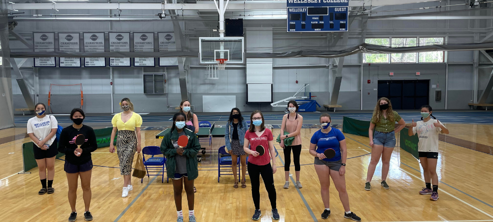 Students posing with ping pong paddles in front of a ping pong table