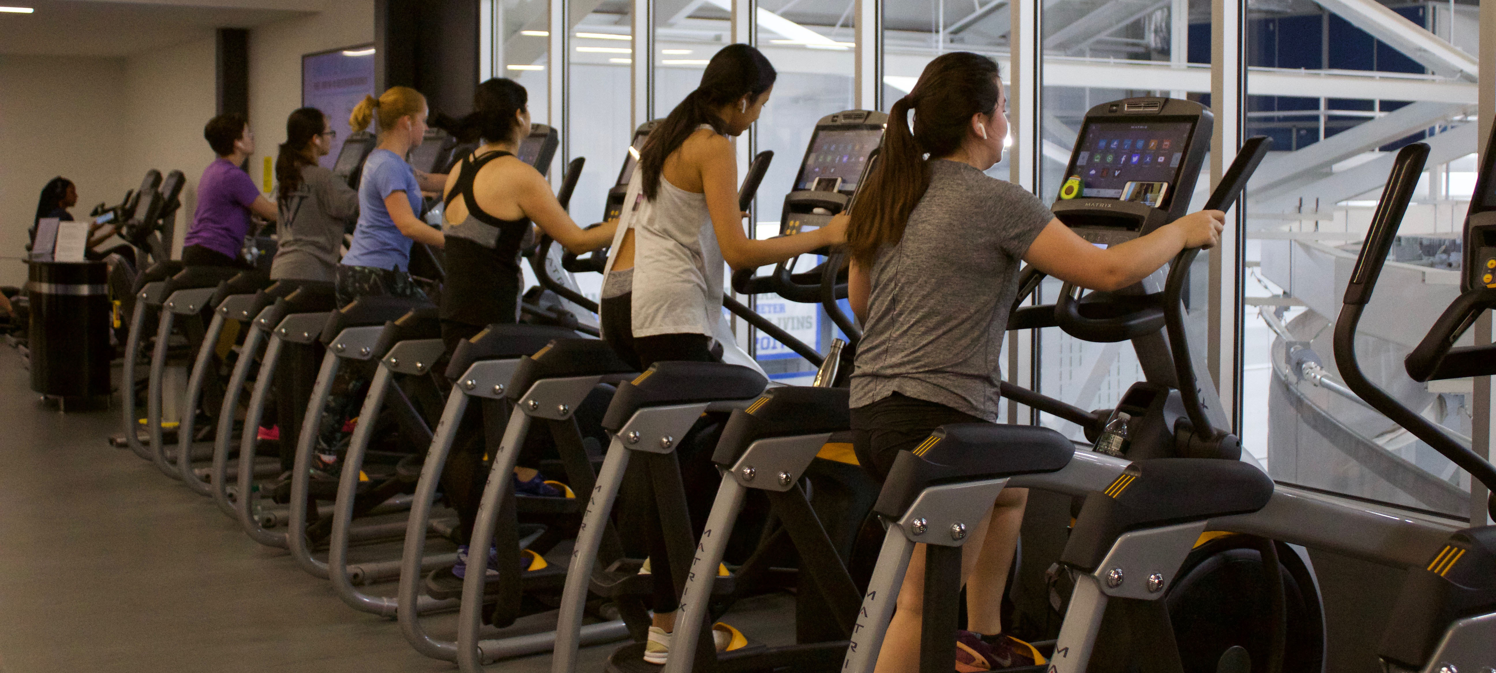 The ellipticals are filled with exercising students facing away from the camera. 