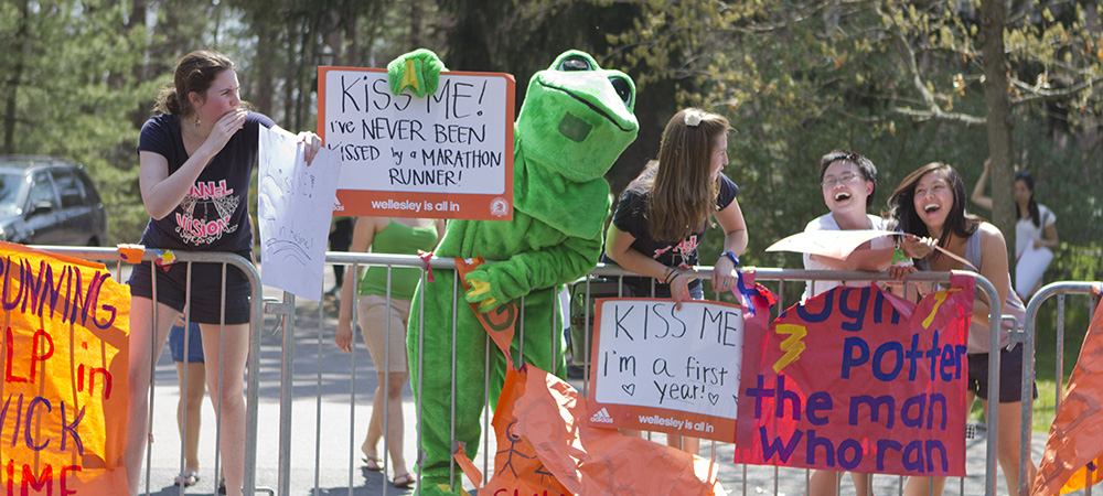 Students cheering on the runners in frog costumes and with creative signs 