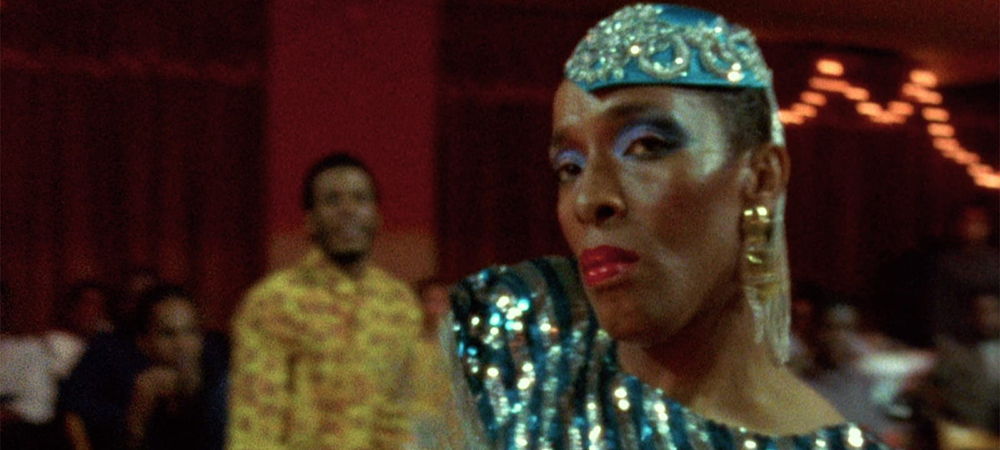 A still from the film Paris is Burning, a performer in drag gives the camera a look while competing in a ball