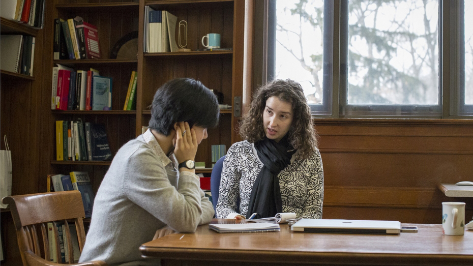 Two students discussing at a library table.