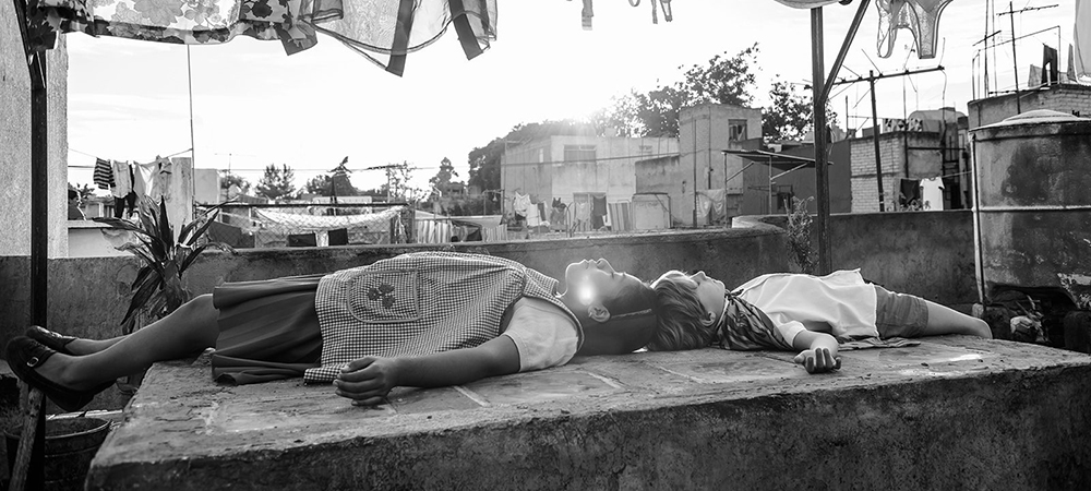 A still from the film Roma. A woman and a boy lie on a roof under a clothesline.