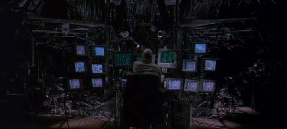 A still from the film the Matrix. A person looks at a stack of screens. 