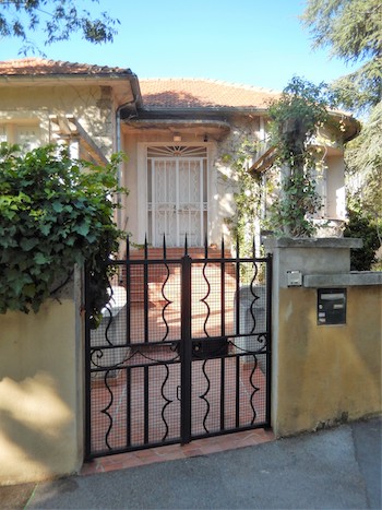 A short black metal gate in front of the entrance to a white and tan Provence-style house.