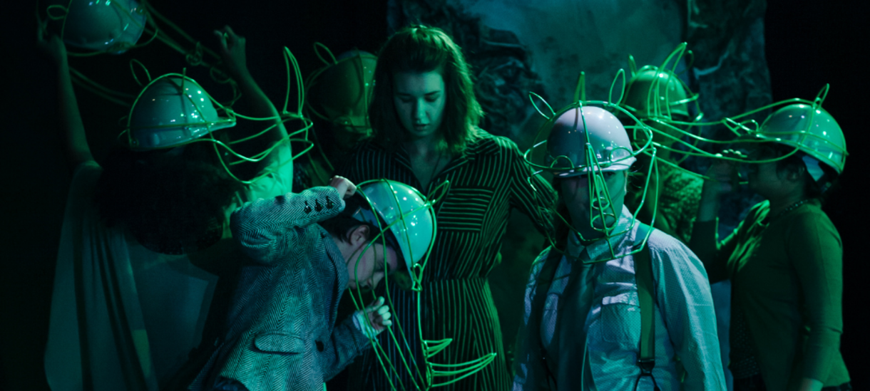 Actors in green lighting and rhino headpieces.