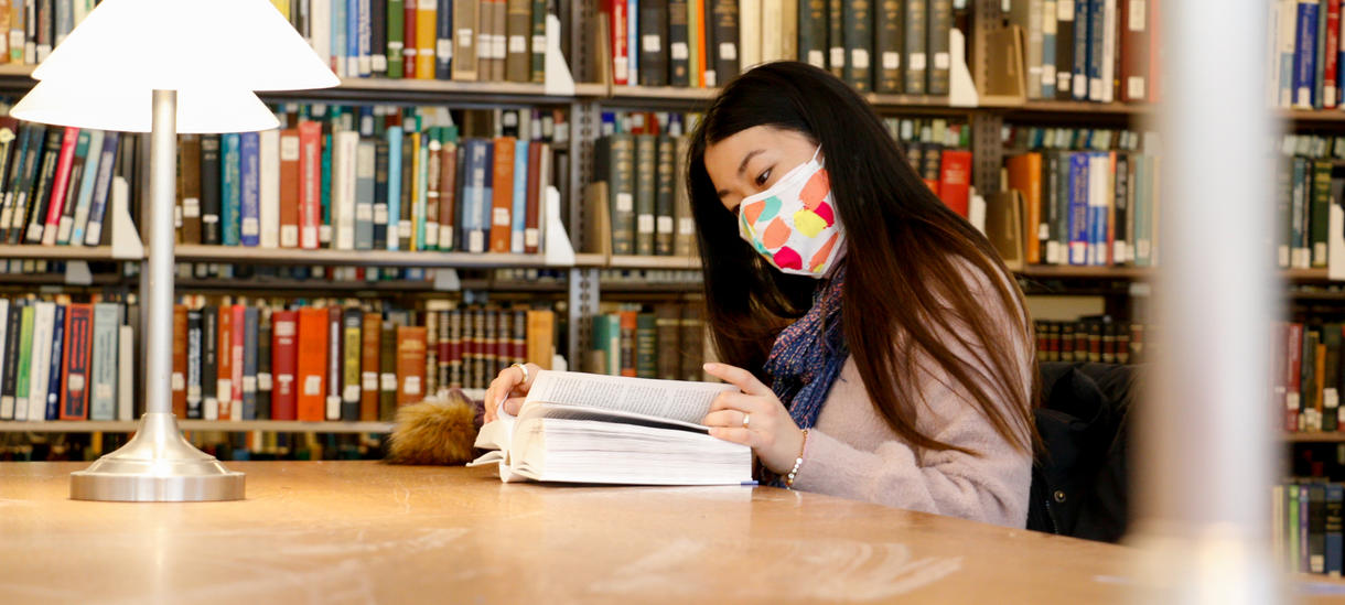 Student reading in the library in Fall 2020, wearing a colorful mask for COVID protection of herself and others.