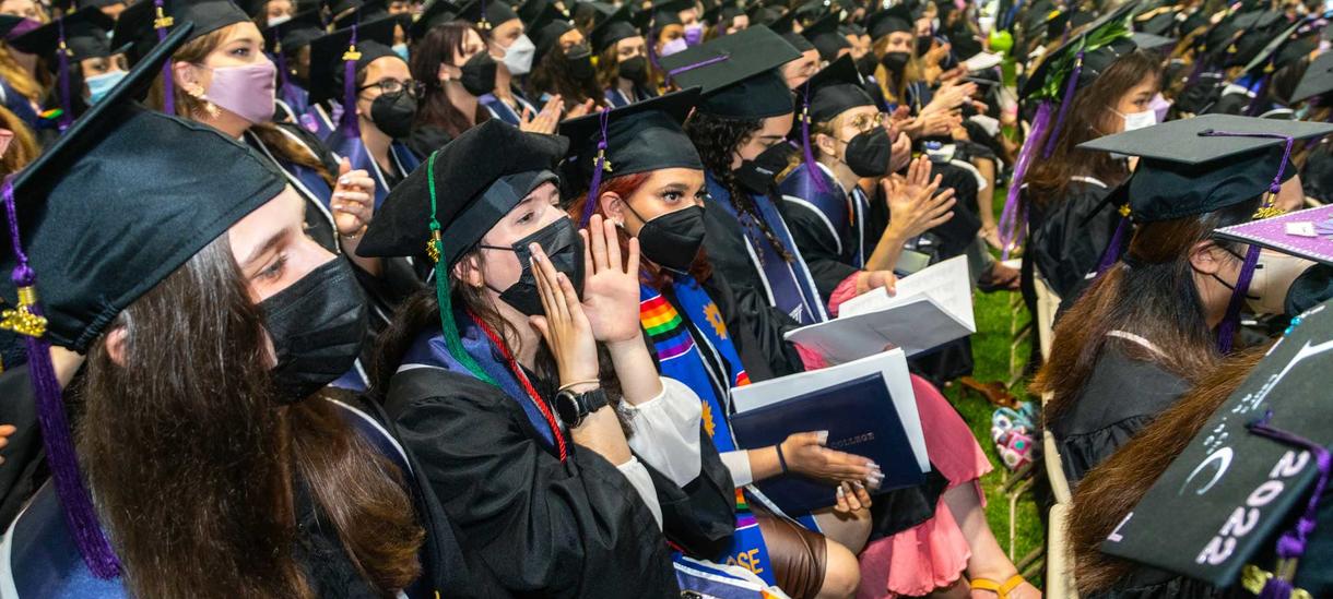 students in their caps and gowns applaud and cheer from the audience