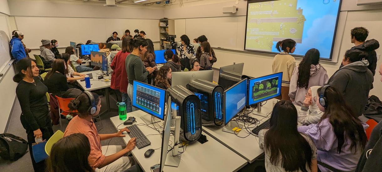 Students clustered around many computers in a lab. Many different video games are visible on the screens.