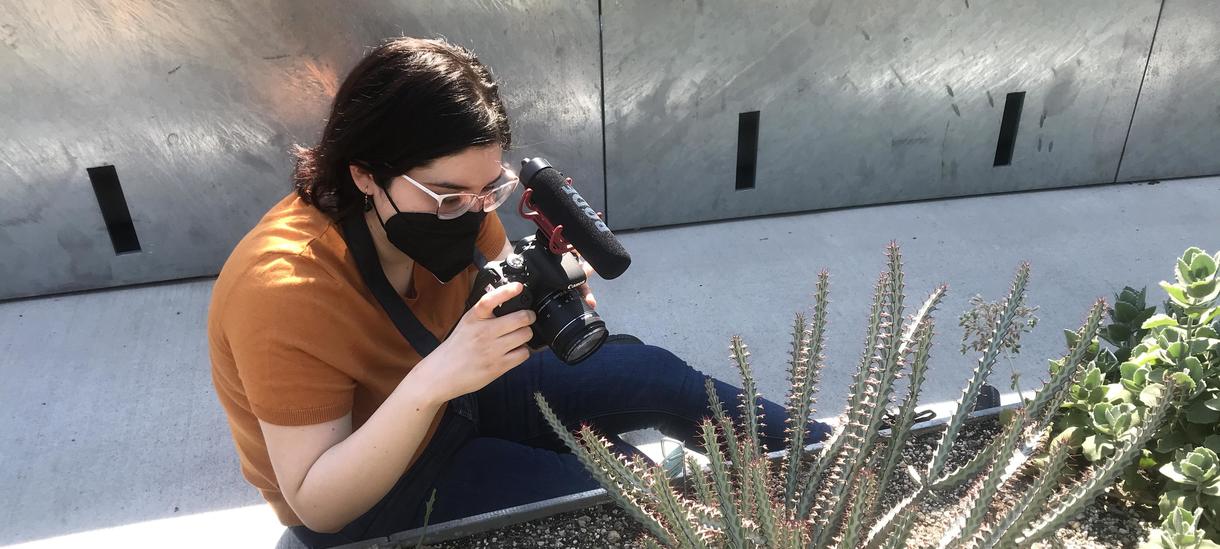 Student with video camera filming plants in the greenhouse