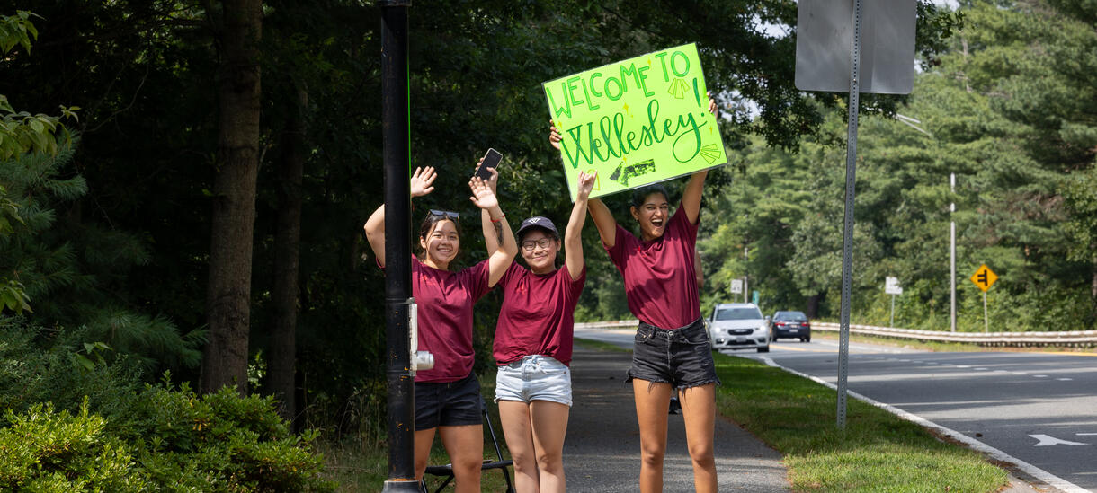 Three orientation leaders welcoming entering students with a neon green welcome sign. 