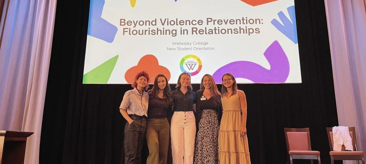 Students smiling in front of projector that reads "Beyond Violence Prevention: Flourishing in Relationships"