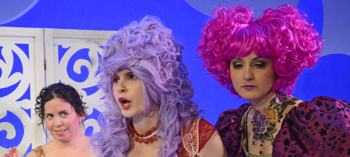Three actresses in large brightly colored wigs.