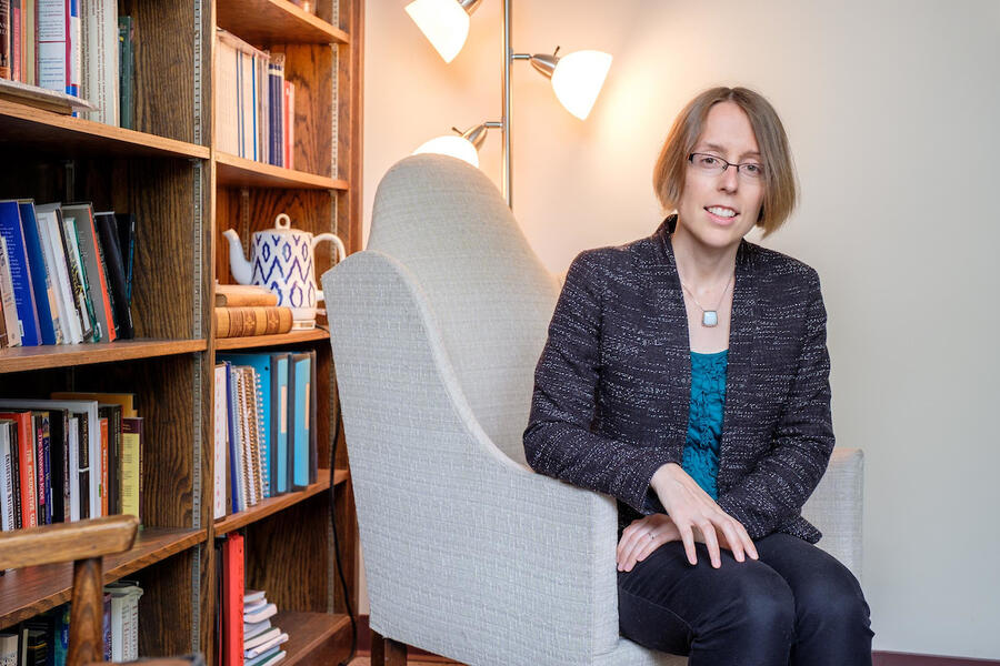 Christina Carroll sits in a light gray chair in front of a bookshelf.
