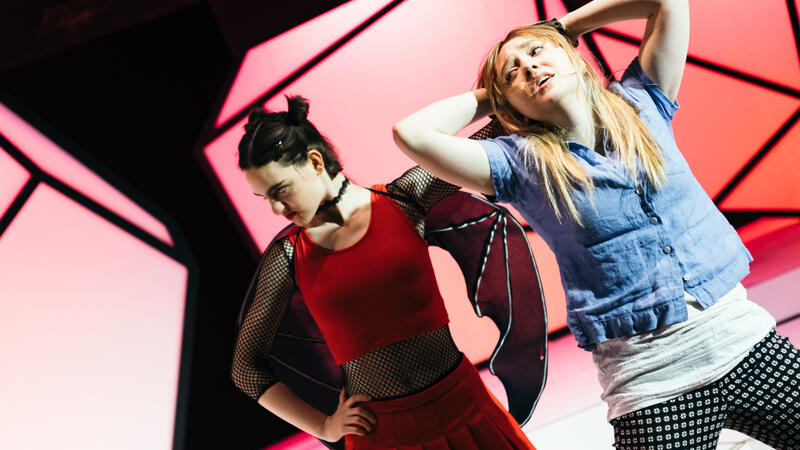 actor dressed as red devil pulling hair of actor in normal clothes