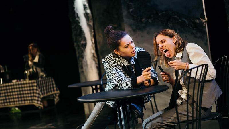 two actors in black white and grey clothing at cafe table