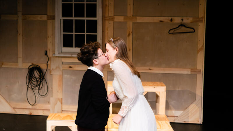 Actor in tux and actor in wedding dress kissing