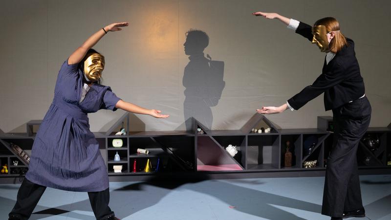 two actors in masks in front of shadow puppet