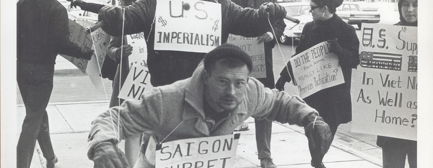 Protesters carry signs and act out "Saigon Puppet" demonstration in front of Wichita City Building.