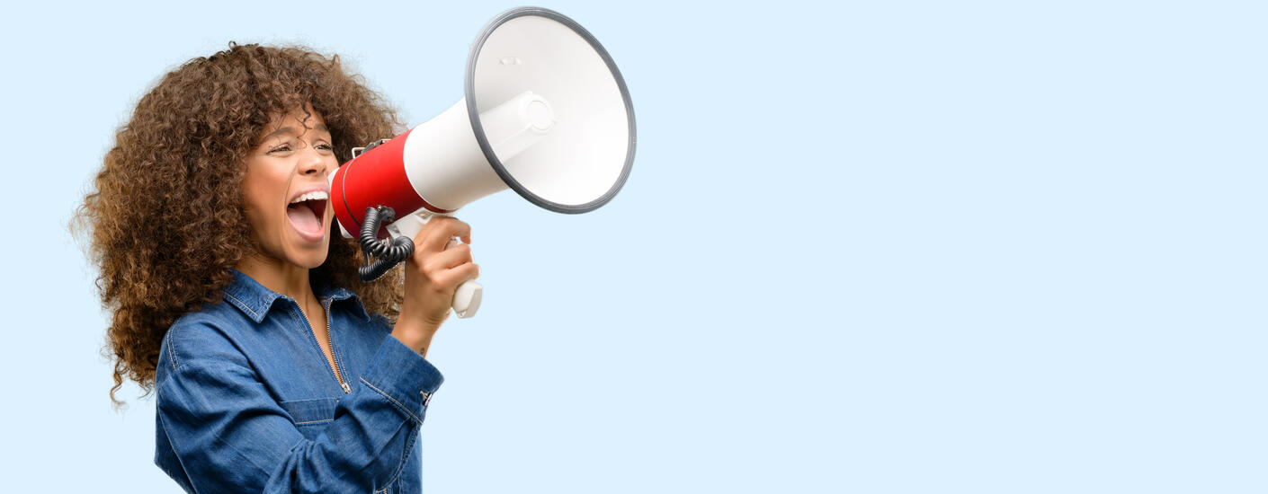 Woman wearing blue jumpsuit shouting into a megaphone