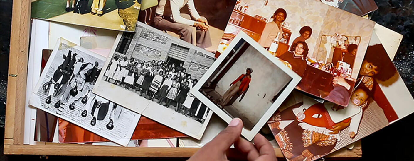 image of a hand holding an vintage photograph. Behind the hand is a wooden box filled with other vintage photographs of people