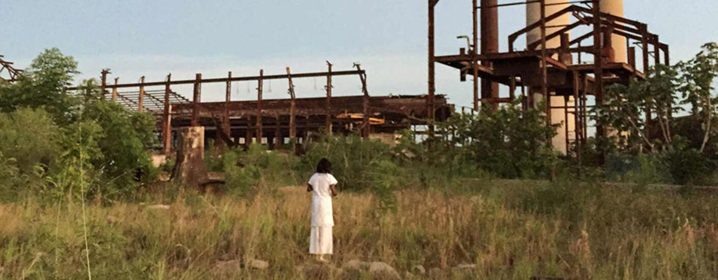a woman standing in a field looking at an industrial building
