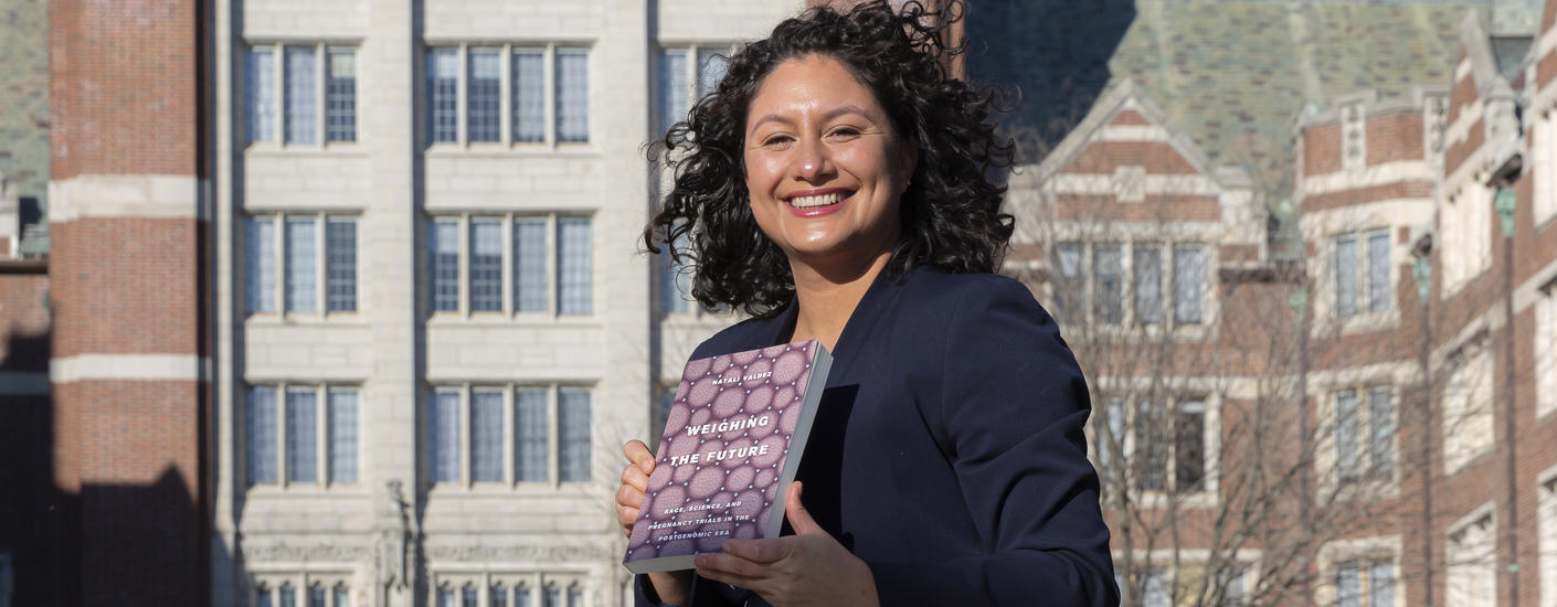 Prof. Natali Valdez, holding a copy of her new book in front of Tower Court