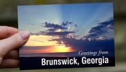 Hand holds a postcard that reads "Greetings from Brunswick, Georgia"