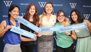 Alumnae hold "Wellesley Welcome" signs in front of a blue backdrop 